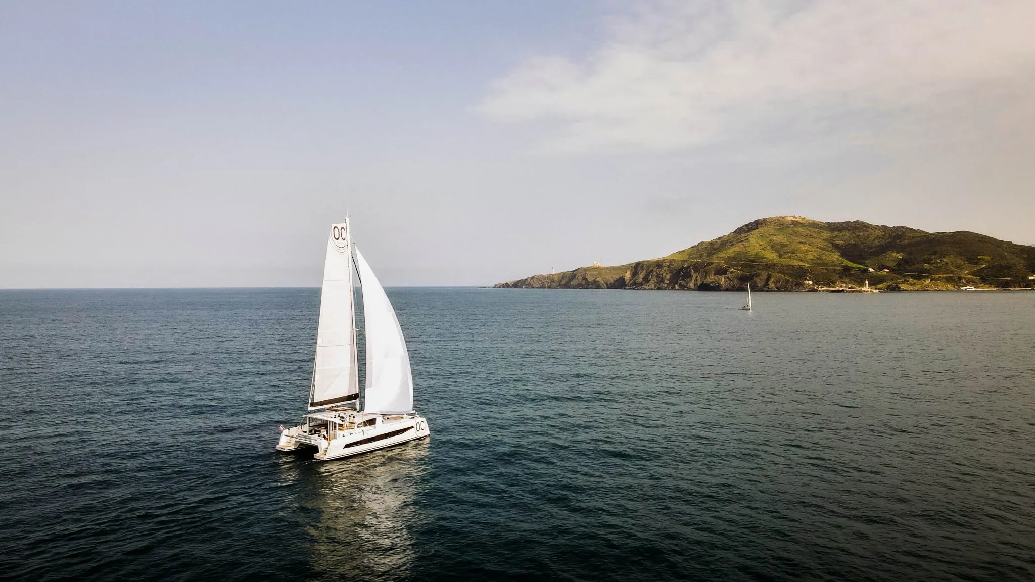 Catana catamaran sailing on open water with coastline in the background