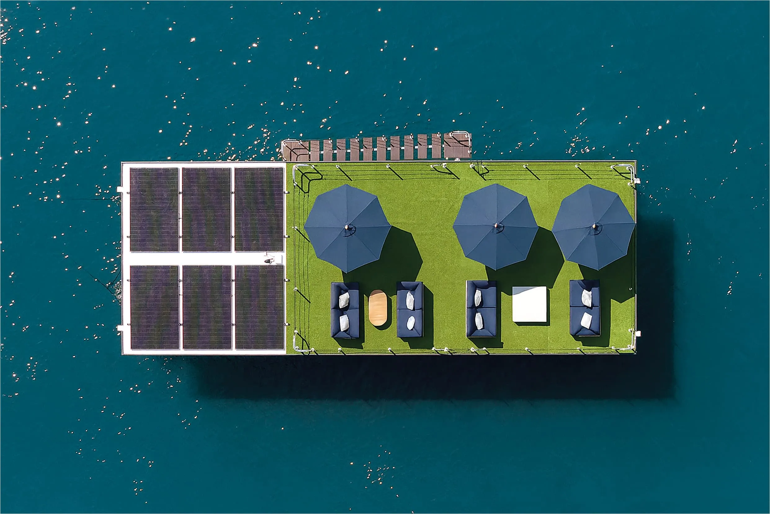 Top view of a floating platform rooftop with solar panels, lounge seating and parasols above open water
