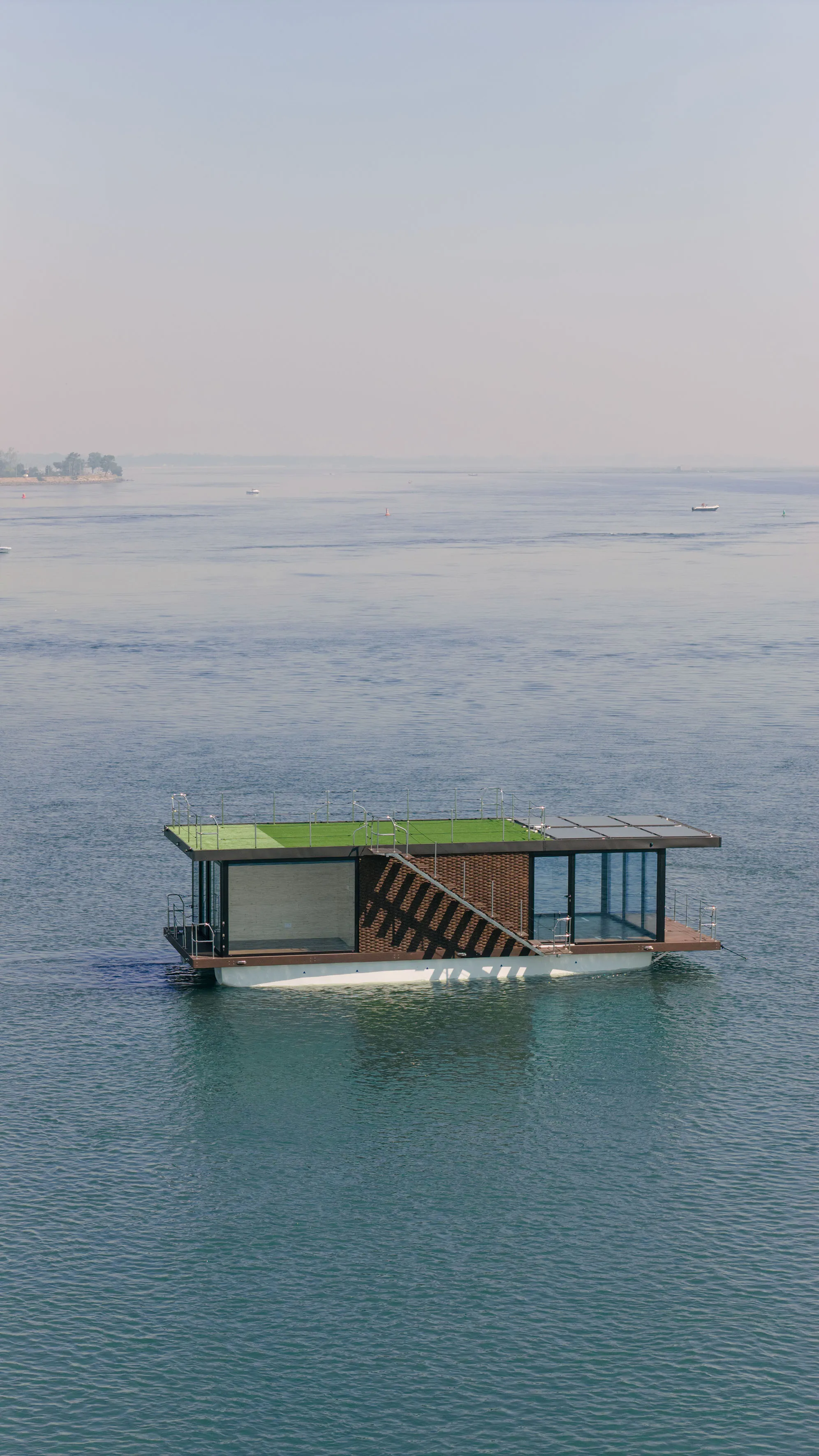 Floating villa platform on open water with rooftop access and full glass facade, photographed during daytime.
